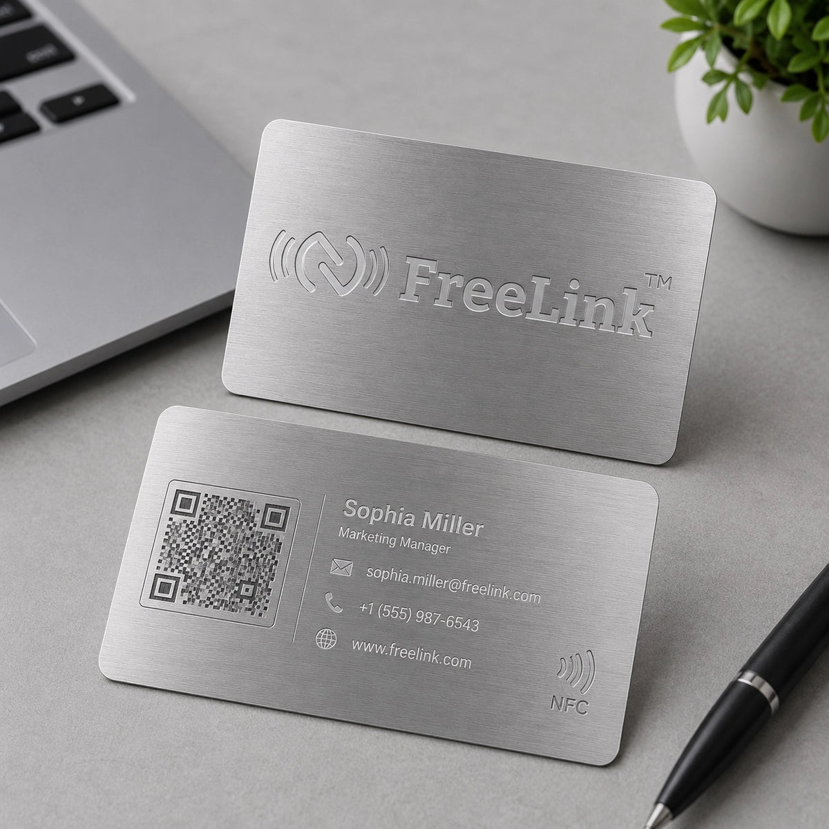 Premium Freelink Silver NFC Metal Business Card with laser-engraved FreeLink logo on front side and QR code name, phone no, emaill id displayed on backside n a modern office workspace. Durable stainless steel NFC card for digital networking and smart business connections.